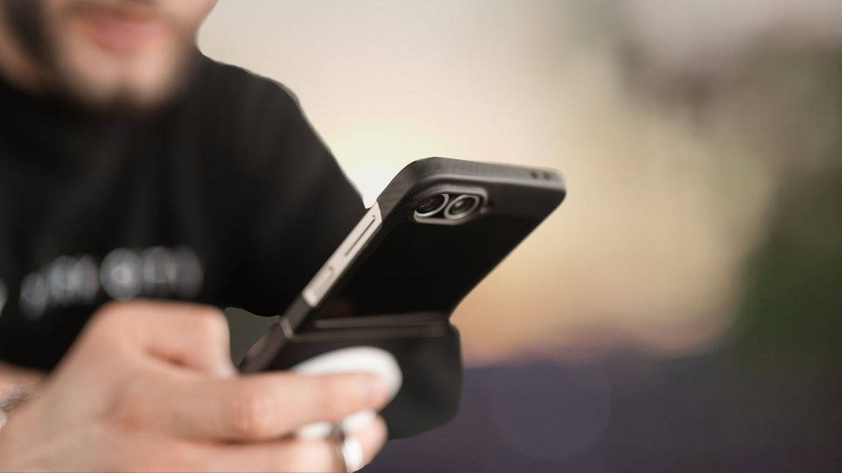 blurry background showing man holding a phone using Galaxy z flip 7 FE black matter aramid case