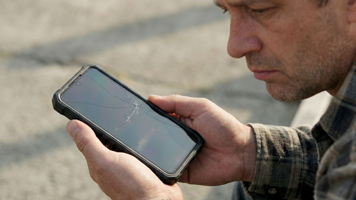 Sad man holding Galaxy S26 Plus in a rugged case with a broken screen