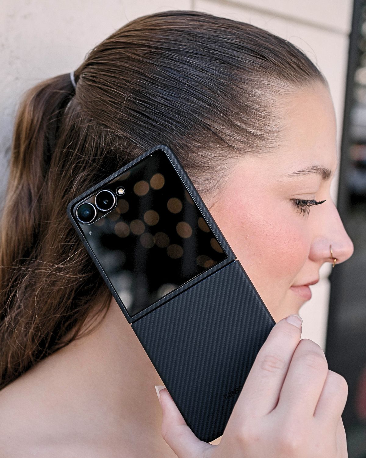 A woman holds a half-folded Z Flip 7 with a carbon fiber case to her ear.