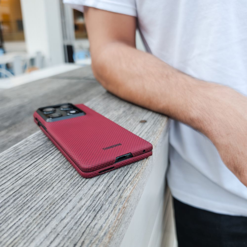 close shot of motorola razr fold with red case laying on a surface near a man's arm