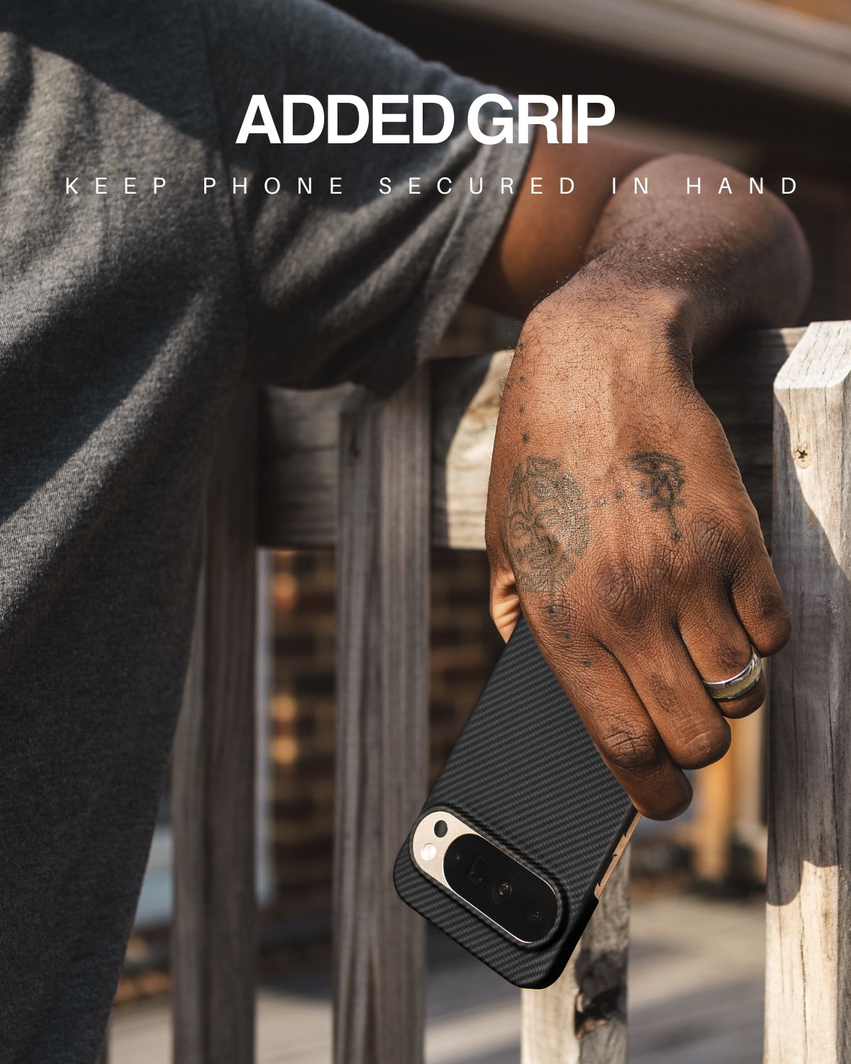 A man with a tattoo holds a phone with a black, textured Pixel 10 Pro xl case, resting his hand on a wooden railing to demonstrate the case's added grip.