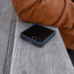 galaxy z flip 8 case fitted on a folded phone, resting flat on a rustic wooden bench next to a person wearing a brown jacket.
