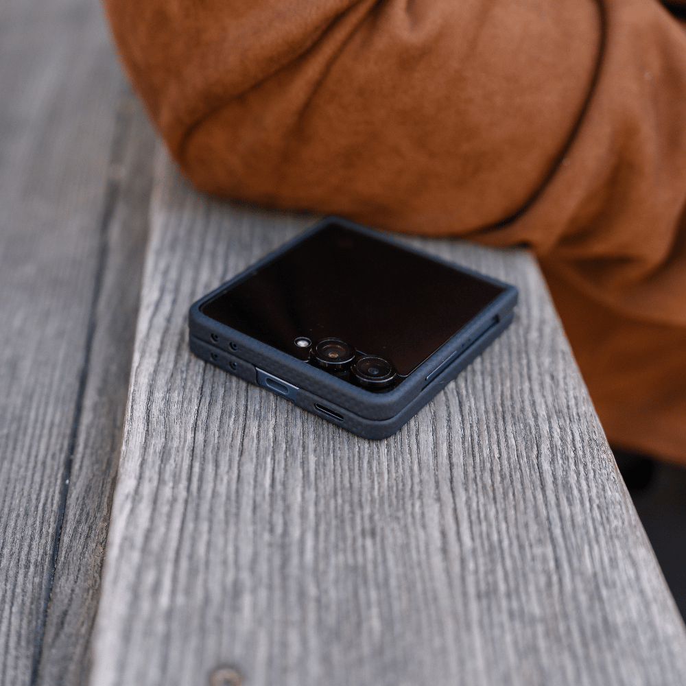 galaxy z flip 8 case fitted on a folded phone, resting flat on a rustic wooden bench next to a person wearing a brown jacket.