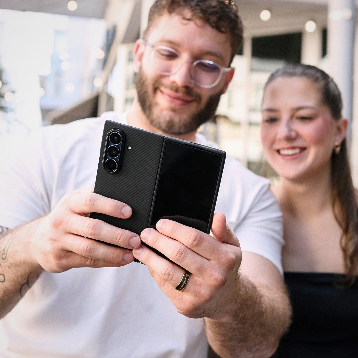 A man holding a Samsung Galaxy Z Fold 8 Ultra in a slim, black textured aramid fiber case, showing the camera module and cover screen.