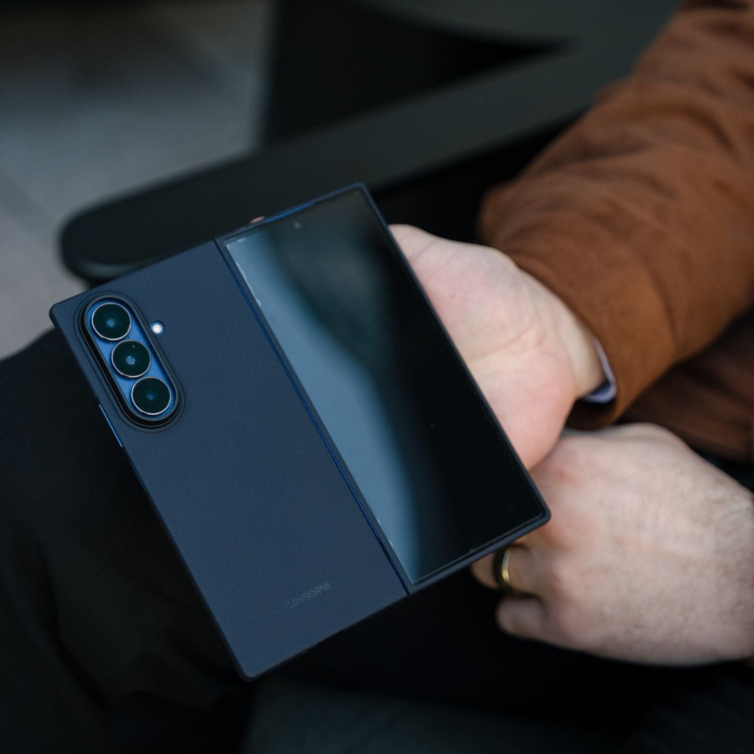 Hands holding a partially folded Samsung Galaxy Z Fold 8 Ultra in a navy blue aramid fiber case, showing the camera module and front screen.