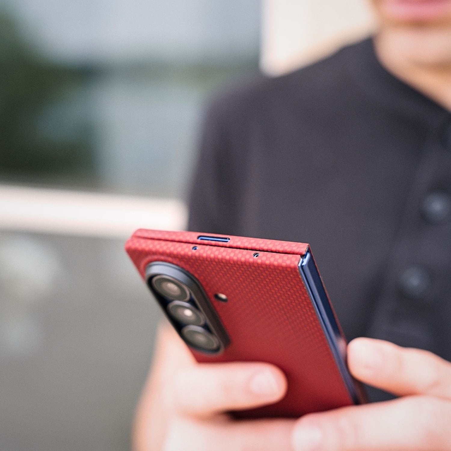 Close-up of a person holding a galaxy z fold 8 ultra  in a red aramid fiber case, showing the top speaker cutouts and camera module.