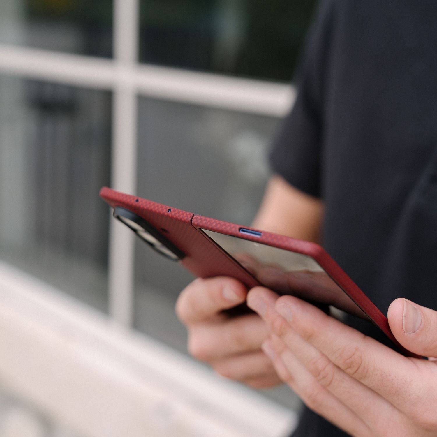 Close-up of a person holding an unfolded galaxy z fold 8 ultra in a red aramid fiber case, showing the top speaker cutouts and camera module.