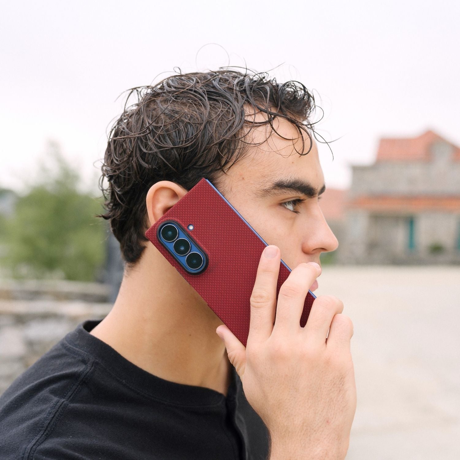 A man holding a Galaxy Z Fold 8 Ultra in a red carbon fiber-style case to his ear as if making a call.