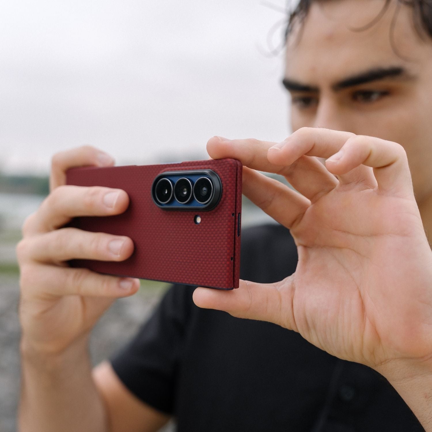 A man holding a Galaxy Z Fold 8 Ultra in a red aramid fiber case horizontally to take a photo, showing the triple camera cutout.
