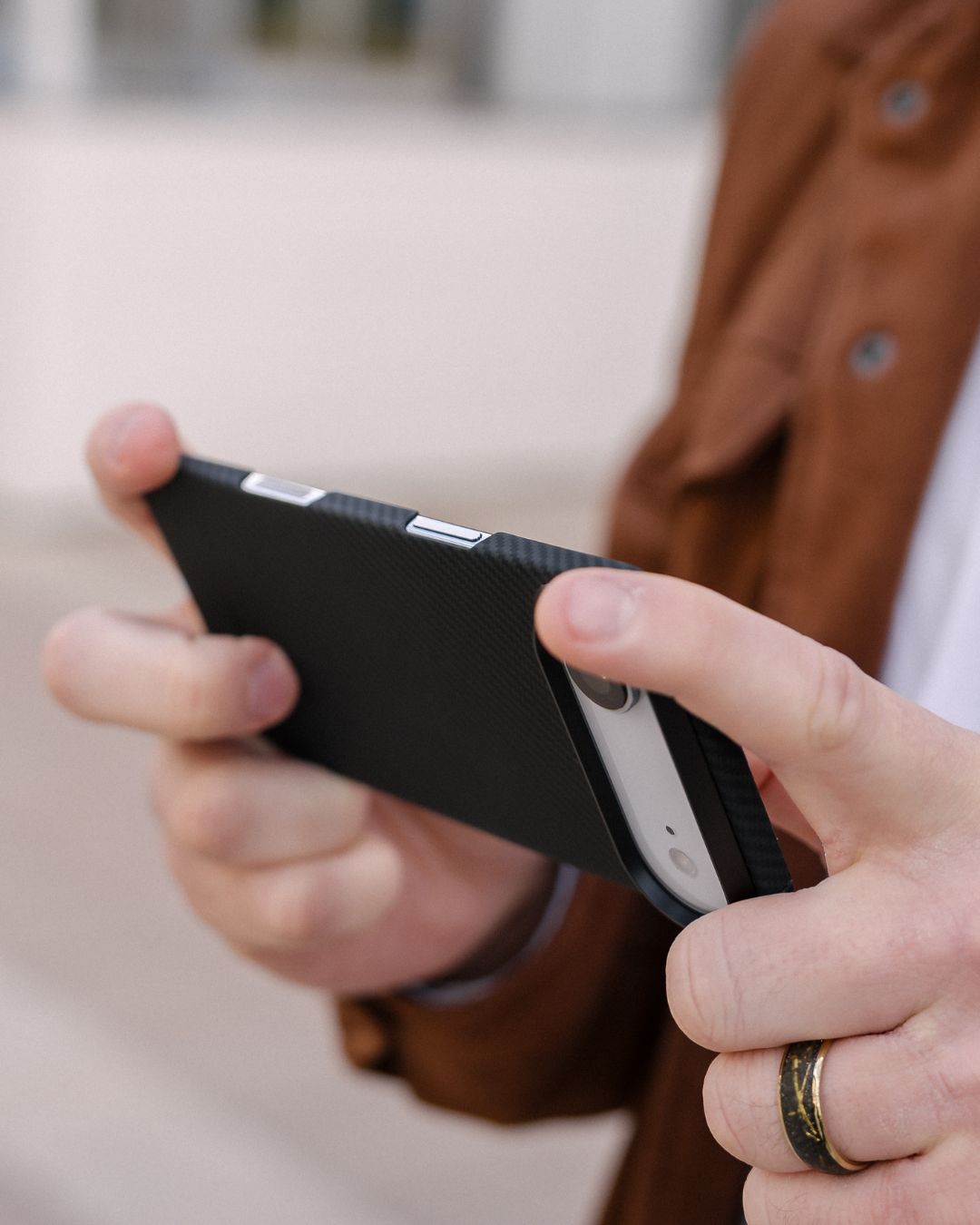 Person holding a smartphone with a black iphone air case, wearing a brown jacket.