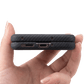 A close-up of a hand holding a slim black carbon-fiber-textured motorola razr ultra 2026  phone case from the bottom edge, showing two USB-C ports and small camera cutouts against a white background.