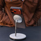 Magsafe stand with a iPhone 17 pro max with a phone on top, placed on a dark surface with a blurred brown jacket in the background.
