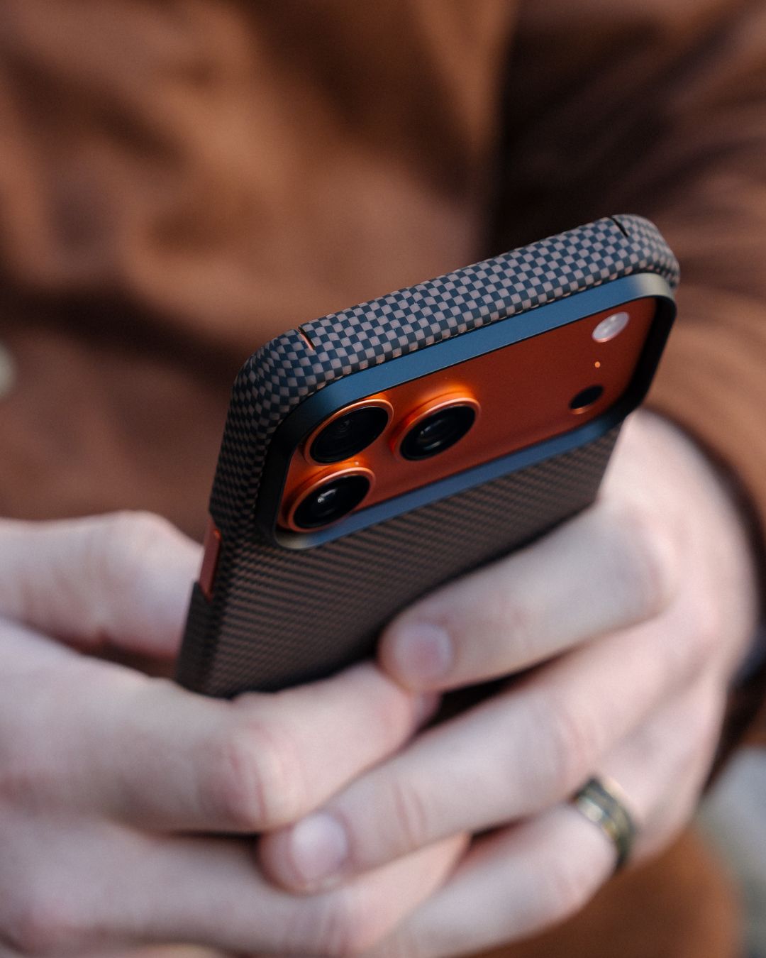 Person holding a phone with a textured iPhone 17 pro max case, blurred background