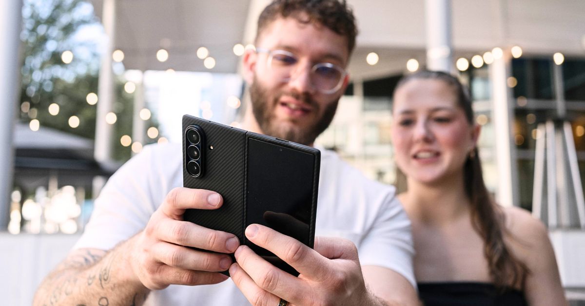 A man and a woman look at a half-folded Galaxy Z Fold 7 with a black carbon fiber case, which the man is holding.