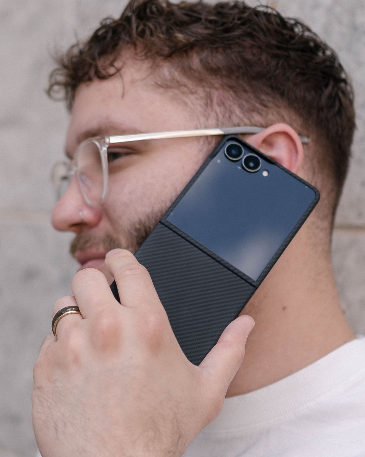 A man on a phone call holds a Samsung Galaxy Z Flip 7 with a two-part, thin carbon fiber case.