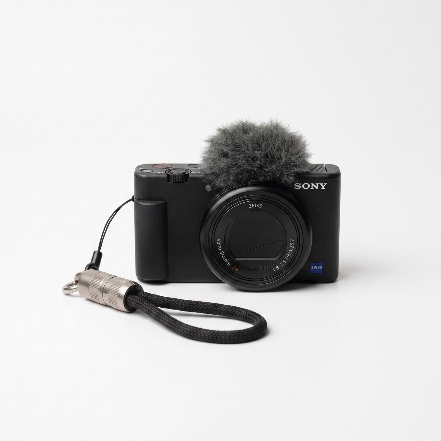 Sony ZV-E T3 camera in black with a gray furry microphone windscreen and a black wrist strap with a silver metal connector, photographed on a clean white background.