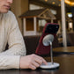 Crimson red iPhone 17 Pro Max MagSafe case attached to a silver magnetic desk stand with a man in a cable-knit sweater.