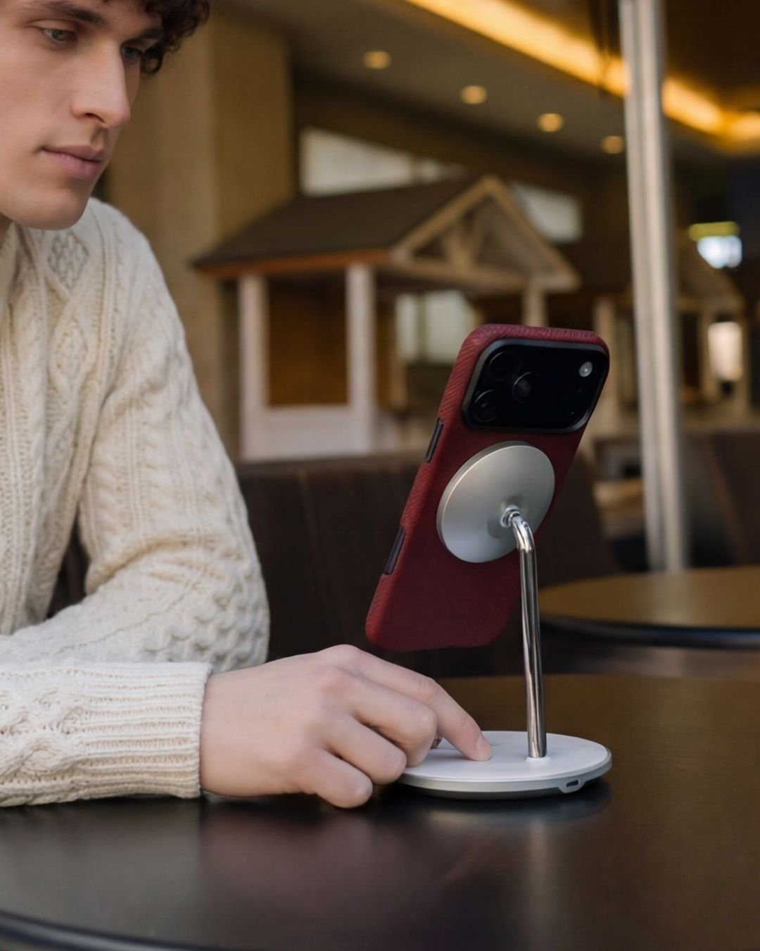 Crimson red iPhone 17 Pro Max MagSafe case attached to a silver magnetic desk stand with a man in a cable-knit sweater.