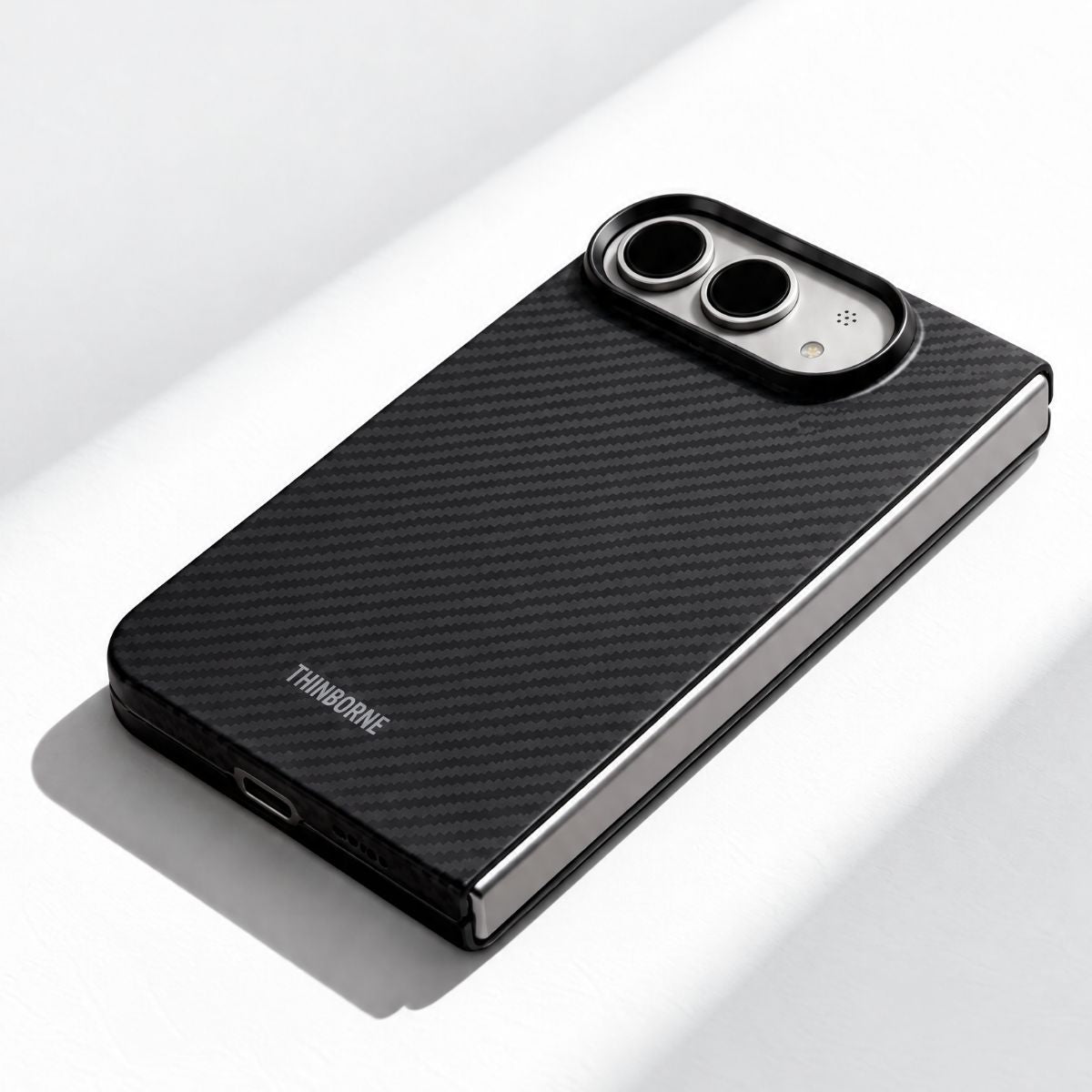A black carbon fiber iPHONE DUO phone case with a silver metallic edge, shown from an angled perspective on a clean white surface. The brand name 'THINBORNE' is printed in white near the bottom left of the case.