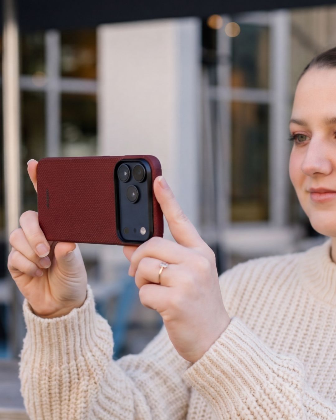 Woman taking a photo in landscape mode with an iPhone 17 Pro Max in a rugged deep red textured case.