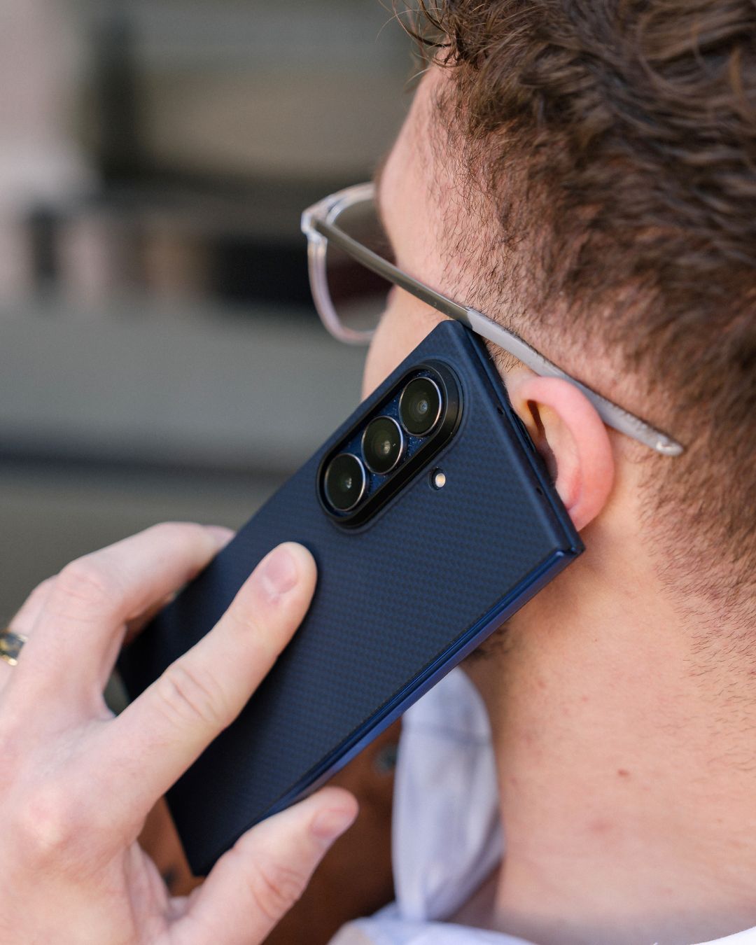 Person holding a blue galaxy z fold 7 case on the phone close to their ear with a blurred background