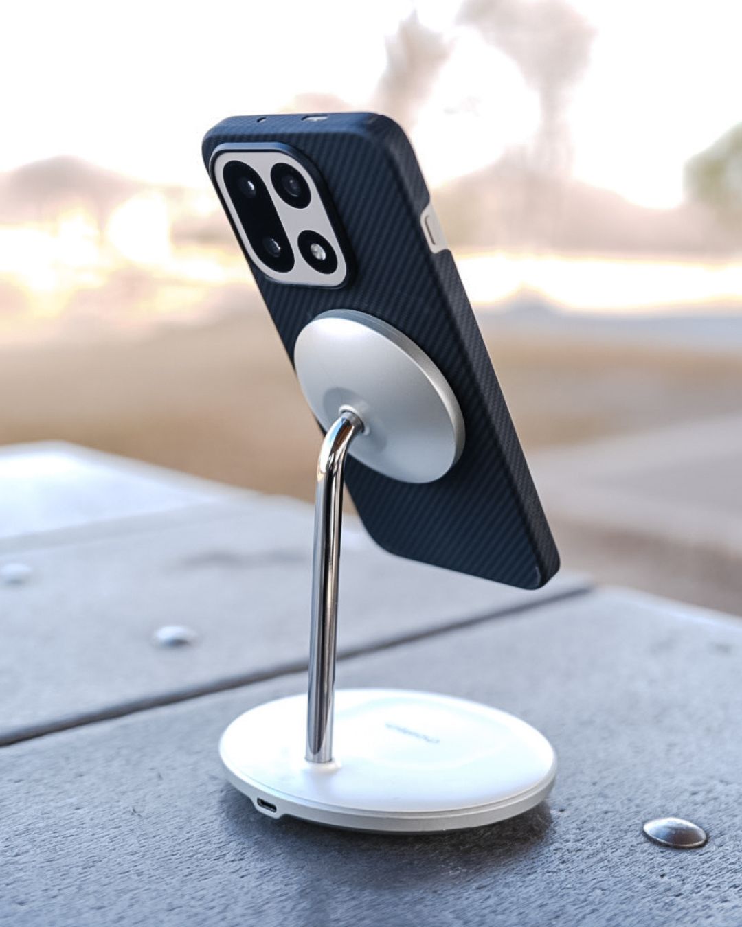 The OnePlus 15 in the aramid fiber case mounted vertically on a sleek, silver MagSafe-style magnetic charging stand, demonstrating the case's strong magnetic attachment and functional compatibility.