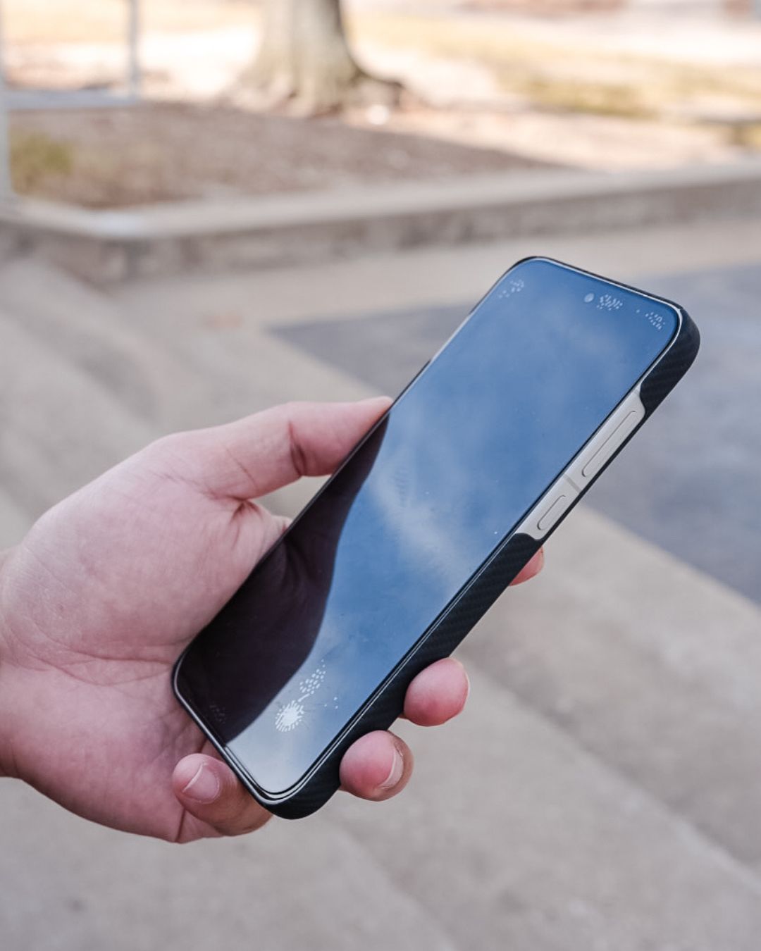A side-view profile of the OnePlus 15 held in a hand, showcasing how the black aramid fiber case maintains the phone's slim aesthetics while providing a textured, grippy surface.