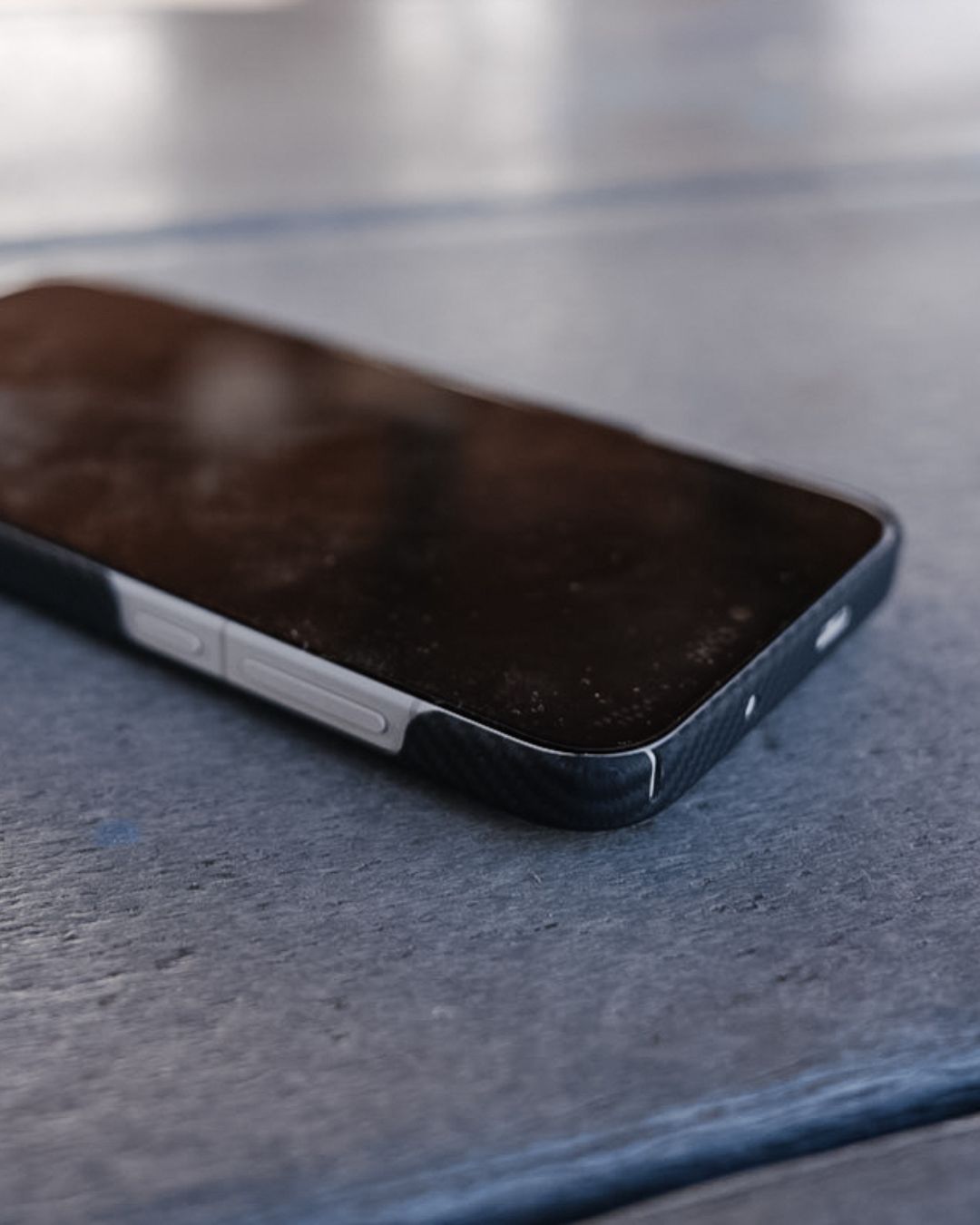 A close-up, angled view of the OnePlus 15 face-down on a wooden surface, highlighting the case's ultra-thin profile and the precise side cutouts that leave the silver volume and power buttons exposed for tactile access.