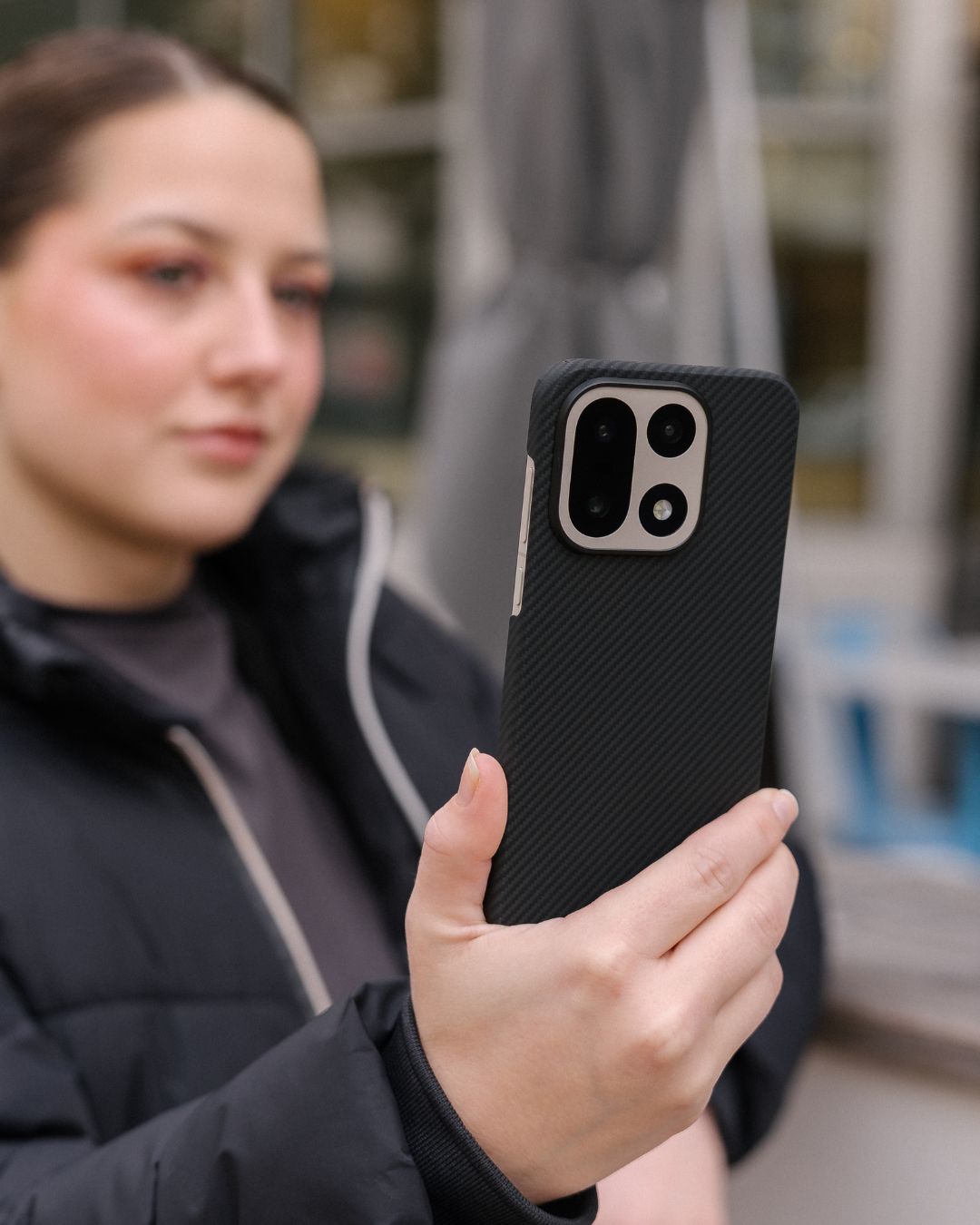 Woman holding a OnePlus 15 in a slim black carbon fiber aesthetic case with precise cutouts for the triple-lens camera system.
