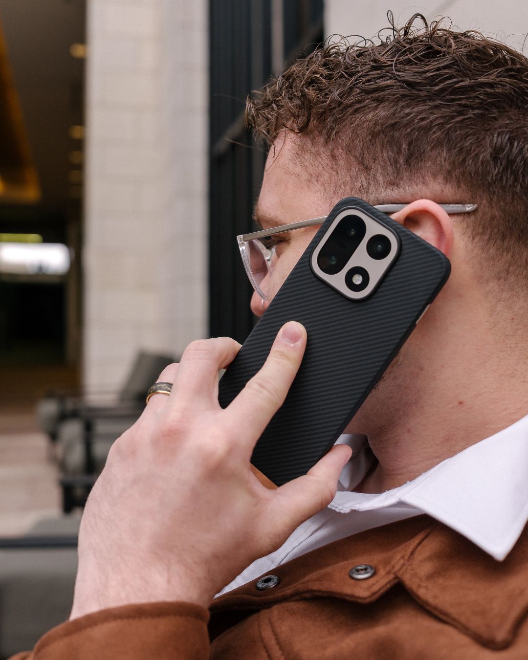 Side profile of a man using a OnePlus 15 in a black aramid fiber case with a reinforced silver camera bezel.
