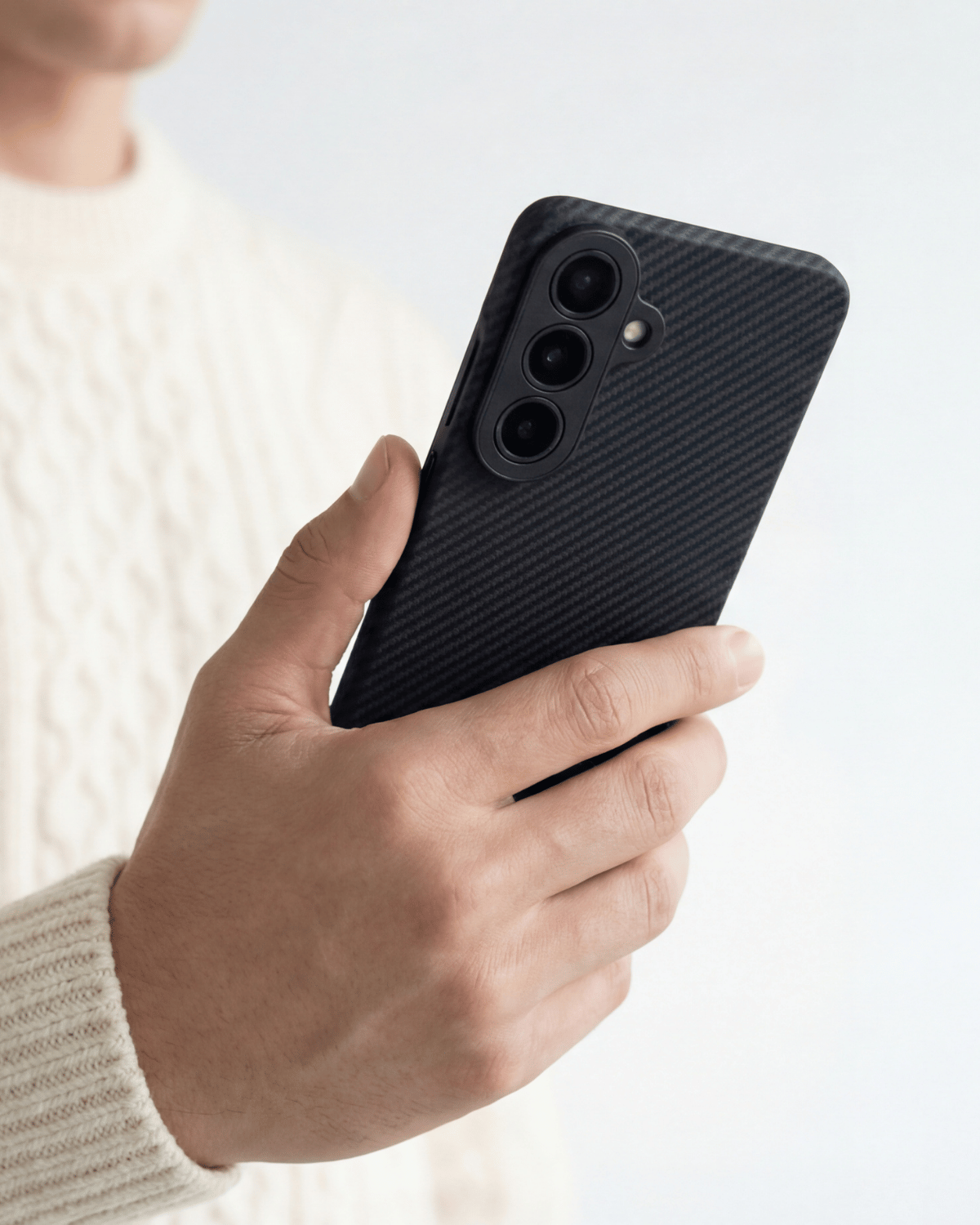 Hand holding a black textured samsung galaxy s26 phone case against a light background