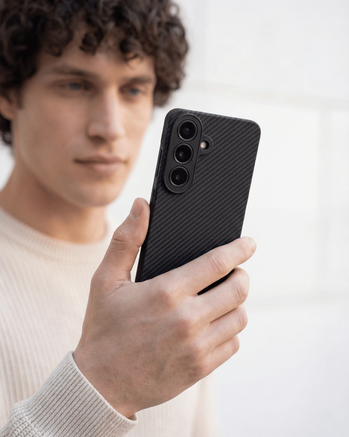 Person holding a black samsung s26 plus phone case with a plain background