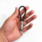 A hand holding a black braided cord keychain with a silver metal cylindrical connector and key ring, shown against a plain white background.