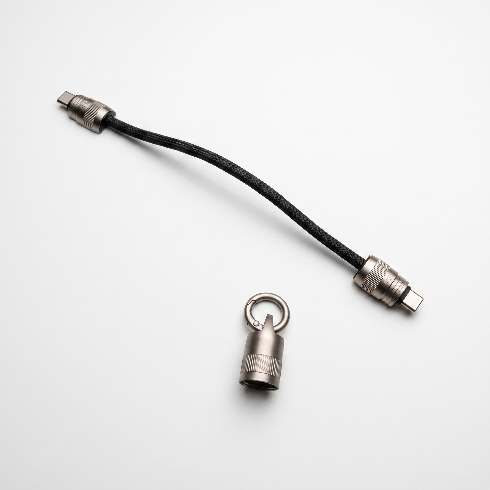 A black braided cable with silver metal connectors, shown on a clean white background alongside a small silver ring-shaped hardware piece.