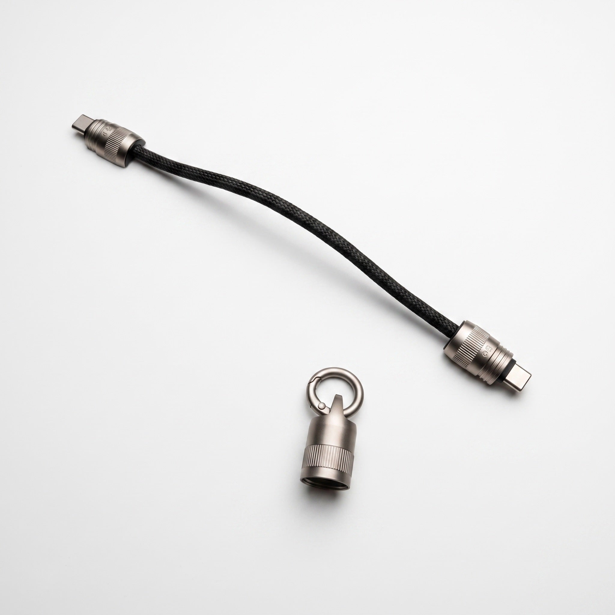 A black braided cable with silver metal connectors, shown on a clean white background alongside a small silver ring-shaped hardware piece.
