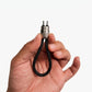 A hand holding a small black braided loop keychain with a silver metal connector and two pins, shown against a plain light gray background.
