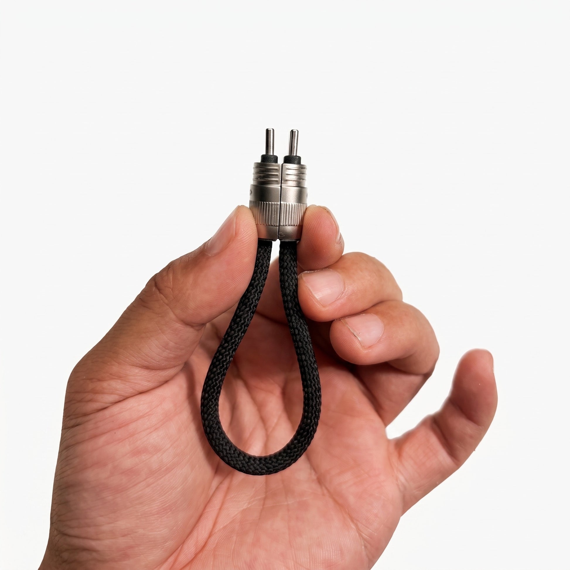 A hand holding a small black braided loop keychain with a silver metal connector and two pins, shown against a plain light gray background.