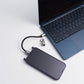 A purple smartphone with a black cable and silver lock connector lies next to an open blue laptop on a clean white surface.